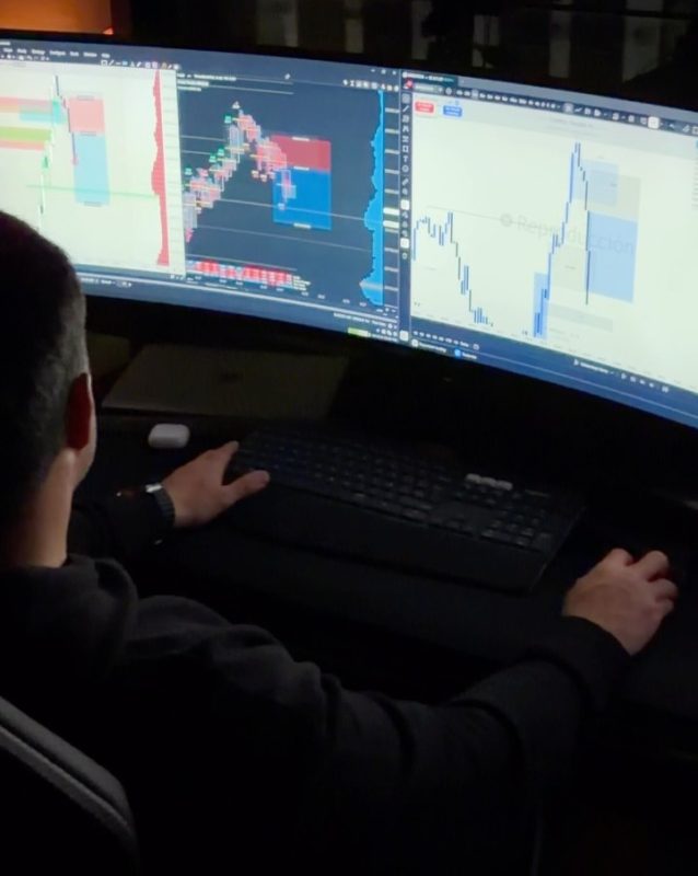 Operador analizando gráficos de trading en tres pantallas de computadora.
