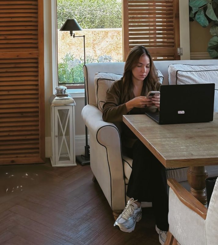 Mujer usando teléfono y laptop en un ambiente de hogar con decoración moderna.