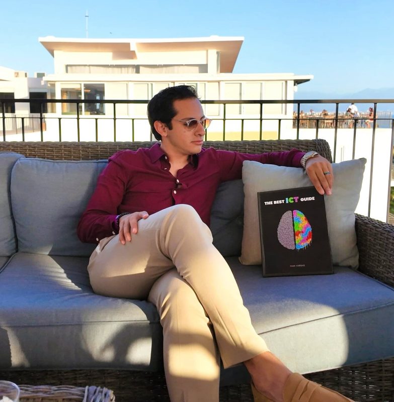 Hombre con gafas en terraza con libro sobre ICT y trading.