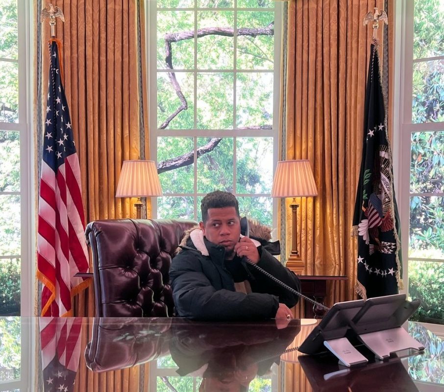 Joven en oficina presidencial con vista a jardines y banderas de EE. UU.